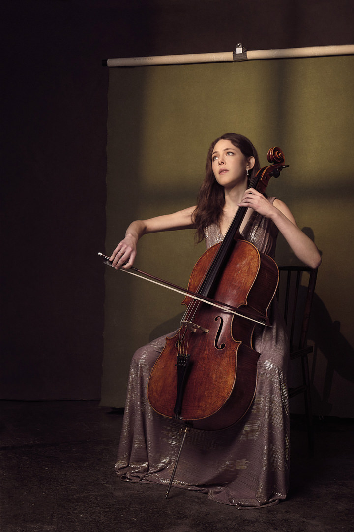 A portrait of a young cellist playing cello in a studio with dramatic lighting.